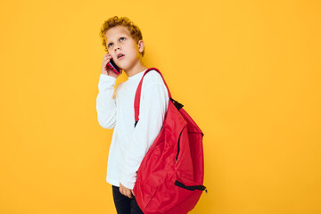 teenager boy with a red backpack calls on the phone yellow background