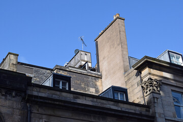 Fototapeta na wymiar Roof Windows & Chimney on Old Classical Style Stone Building against Blue Sky
