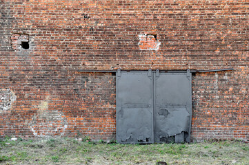 Red brick exterior wall of old factory with iron gates. Old building. Texture, background