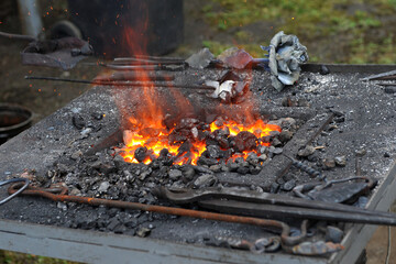   Blacksmith portable furnace with burning coals, tools for hot metal forging workpieces