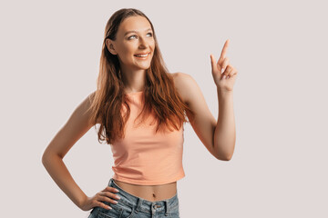 Portrait of a smiling girl pointing finger to the side at on a white isolated background. Positive woman points to an idea, a place for advertising