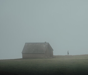 Vertical shot of a female standing alone in front of an aged rural house on a foggy day - Powered by Adobe