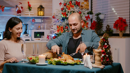 Couple eating chicken at festive dinner on christmas eve celebrating with traditional food and glasses on champagne at home. Man and woman enjoying holiday festivity with food and alcohol