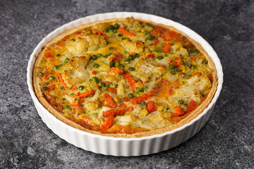 Baked french vegetable pie quiche filled with carrots, peas and cheese on a marble surface