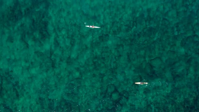 Two single seat Kayaks rowing side by side in calm sea water.
