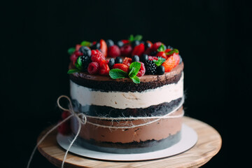 Fruit cake. Cake decorated with berries on a wooden stand on a black background.