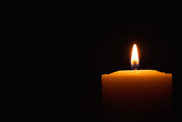 One single light candle burning brightly in the black background.Spiritual candle yellow flame. Flame of candle in the darkness.Copy space.
