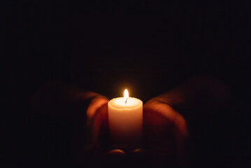 Hands holding burning candle in dark like a heart.Selective focus,black background.Copy space.
