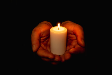 Hands holding burning candle in dark like a heart.Selective focus,black background.
