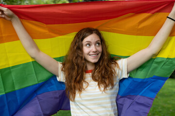 Cinematic shot of happy young red hair woman carrying flag of LGBT rainbow symbol and smiling in...