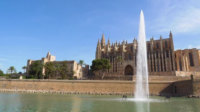 Pan over Cathedral (La Seu) and Royal Palace (Almudaina) in Palma de Mallorca with pond and fountain in the foreground - Spain