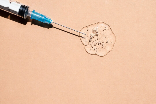 Thin needle in a transparent gel-like liquid with bubbles on a beige background. Top view, place for text.
