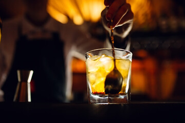 The bartender stirs a spoonful of whiskey with ice in a glass.