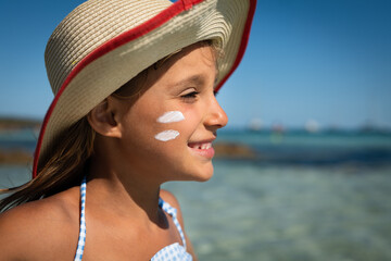 Happy little girl in straw hat is smiling with applied by her mother protective sunscreen or...