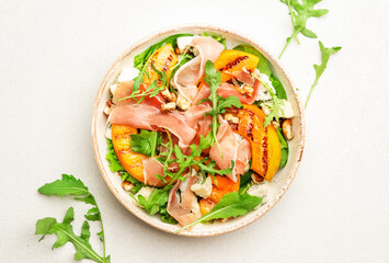 Salad bowl with grilled peach, prosciutto, goat cheese, walnuts and arugula on white background, top view, copy space