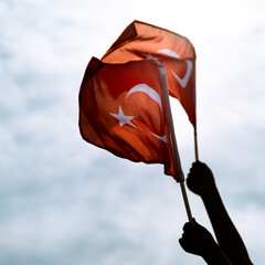 Two Hands holding Turkish flags on a blue and cloudy sky and on the day of liberty Izmir.