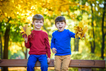happy friends, schoolchildren having fun in autumn park among fallen leaves
