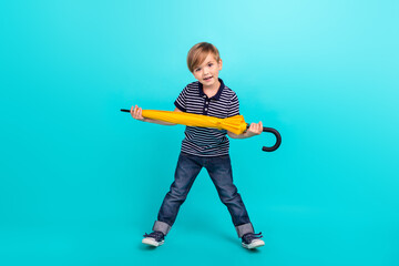 Full body photo of funky little boy hold umbrella wear t-shirt jeans sneakers isolated on teal background