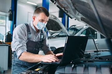 car mechanic using a computer laptop to diagnosing and checking up on car engines parts for fixing and repair.