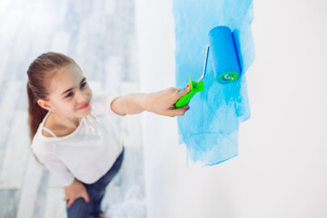 Repair in the apartment. Happy child girl paints the wall with blue paint,