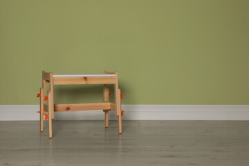 Stylish wooden stool near light green wall indoors. Space for text