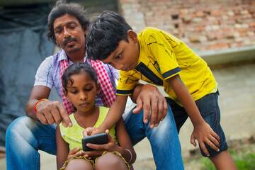 Indian Rural Parent and their two children using mobile phone 