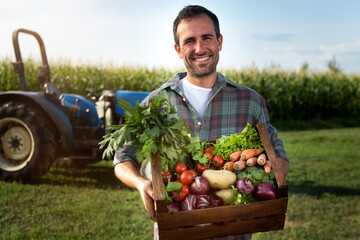 Authentic shot of happy farmer holding basket with fresh harvested at the moment vegetables and smiling in camera on countryside field. Concept:biological, bio products, bio ecology, vegetarian and ve