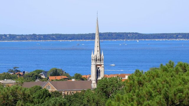 Spire of the Notre-Dame d'Arcachon Basilica and Arcachon bay with some boats sailing on the water