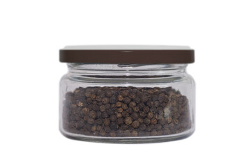 Black pepper in a transparent glass jar. Close-up. Isolated on white background. Condiments and spices.