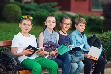 Happy Schoolmates Portrait. Schoolmates seating with books in a wooden bench in a city park and studying on sunny day.