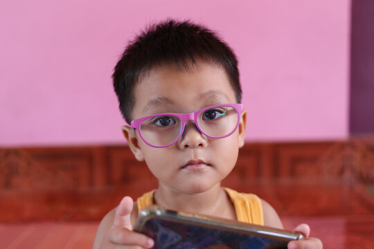 Asian boy wearing glasses and playing on the smart phone.
