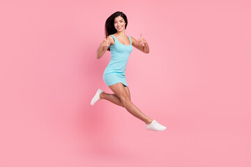 Full size profile photo of funny young lady jump show thumb up wear blue dress sneakers isolated on pink color background