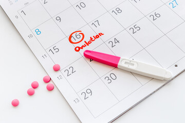 Ovulation home test and pills on calendarwith red mark