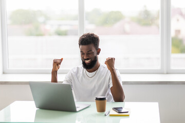 Excited euphoric african winner looking at laptop celebrating online win success achievement result. Black man happy about good news, motivated by great offer or new opportunity, got a job promotion