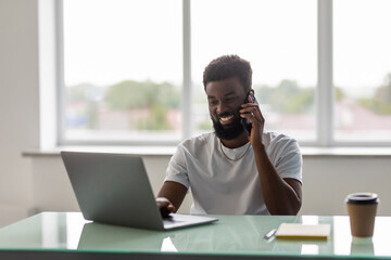 African black man talking on mobile cell phone to clients in office with laptop computer