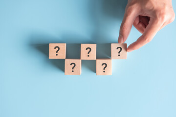 Wooden cube block shape with sign question mark symbol on blue background.