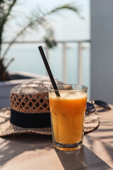 Orange juice, straw hat and glasses in a cafe on the background of the sea.