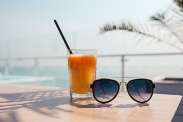 A glass of orange juice and sunglasses on the background of the sea.