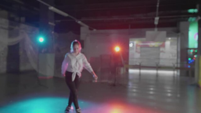 Group of teenage girls roller-skating in dark studio. Millennials rehearse trick moves practicing freeskating style. Young females trying new extreme nightlife lifestyle. Concept of youth, pop culture