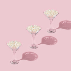 Creative pattern made with white pearls in martini cocktail glass on pastel pink background....