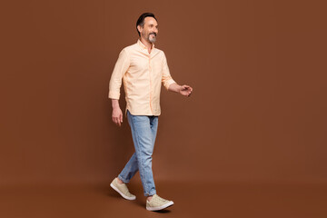 Fototapeta na wymiar Profile photo of cheerful positive guy stroll street wear beige shirt jeans shoes isolated brown color background