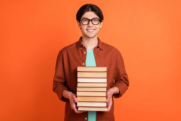 Photo of smiling good mood smart intelligent guy hold pile books college students isolated on orange color background