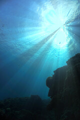 Beautiful and magic underwater photo of rays of light breaking through the surface and the waves. 