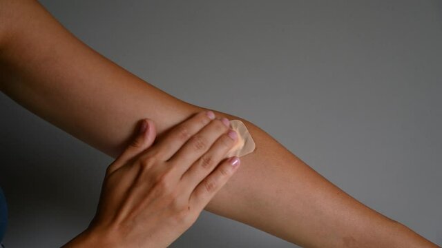 Young woman touching medical patch against gray background, close up. High quality 4k footage