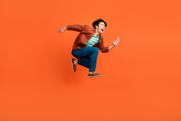 Fototapeta na wymiar Full size profile side photo of happy funky man running in air look copyspace traveling isolated on orange color background