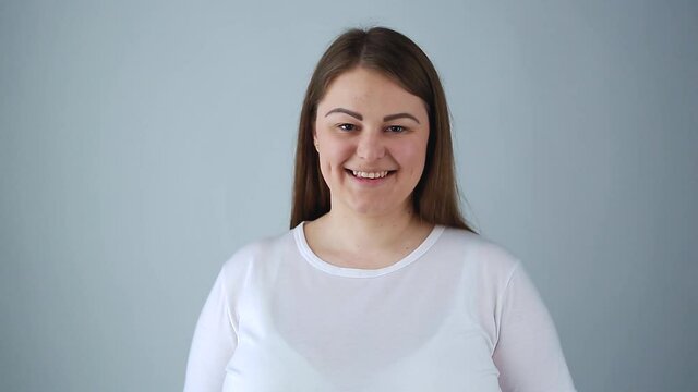 Overweight young woman with happy smile. Friendly plus size model posing for video clip in studio