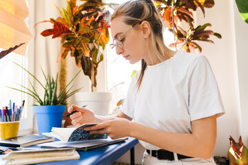 Young white woman in eyeglasses writing down notes while working indoors