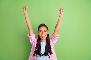 Photo of young cheerful dark skin woman raise fists winner celebrate isolated on shin green color background