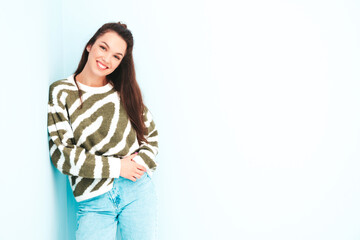 Young beautiful smiling female in trendy winter warm sweater. Sexy carefree woman posing near light blue wall in studio. Positive model having fun indoors. Cheerful and happy