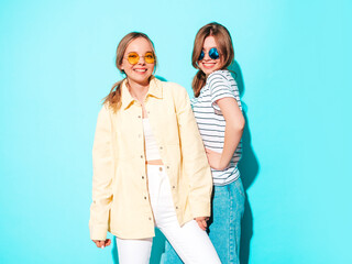 Two young beautiful blond smiling hipster female in trendy summer clothes. Sexy carefree women posing near blue wall in studio. Trendy and positive models having fun